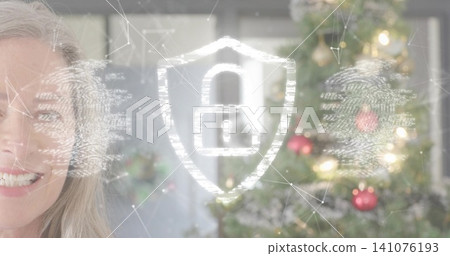 Smiling senior woman in light top at home, showing security graphics and Xmas tree, copy space Smiling senior woman in light top at home, showing security graphics and Xmas tree, copy space 141076193