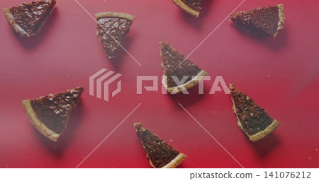 Arranging triangular nutty tart slices on red tabletop showing pastry crusts, nut pieces and crumbs 141076212