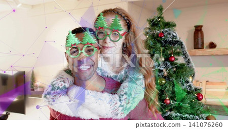 Posing couple wearing green tree glasses and knit sweaters at home with Xmas tree, digital overlay Posing couple wearing green tree glasses and knit sweaters at home with Xmas tree, digital overlay 141076260