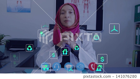 Sitting doctor in white coat scarf clasping hands at desk in clinic with stethoscope floating icons Sitting doctor in white coat scarf clasping hands at desk in clinic with stethoscope floating icons 141076280