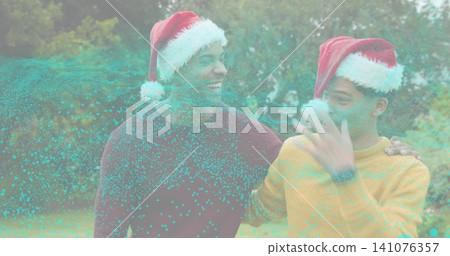 Smiling two men standing close in yard wearing Santa hats sweaters wristwatch and turquoise overlay Smiling two men standing close in yard wearing Santa hats sweaters wristwatch and turquoise overlay 141076357