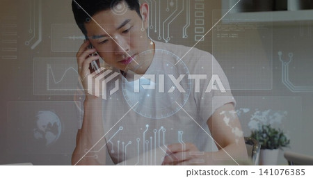 Talking Asian man wearing tee, holding phone, writing with pen on paper at home, HUD overlay Talking Asian man wearing tee, holding phone, writing with pen on paper at home, HUD overlay 141076385