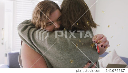 Hugging two women at home, wearing knit sweater, tank top, holding red key fob, confetti floating Hugging two women at home, wearing knit sweater, tank top, holding red key fob, confetti floating 141076387