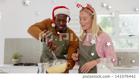 Whisking batter, couple in green aprons, Santa hat, candy-cane headband, bowl and whisk in kitchen Whisking batter, couple in green aprons, Santa hat, candy-cane headband, bowl and whisk in kitchen 141076442