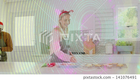 Decorating woman in gray apron and red-and-white headband at kitchen island with cooling rack Decorating woman in gray apron and red-and-white headband at kitchen island with cooling rack 141076491