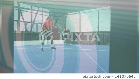 Holding paddle, male in orange and female in black tank preparing return shot inside covered court Holding paddle, male in orange and female in black tank preparing return shot inside covered court 141076643