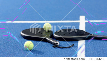 Showing black padel paddles resting on blue court near white lines with three balls and strap 141076646