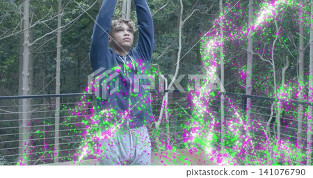 Raising arms, man wearing navy hoodie, grey sweatpants on deck by cable railing with magenta CGI Raising arms, man wearing navy hoodie, grey sweatpants on deck by cable railing with magenta CGI 141076790