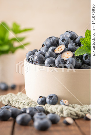 A ceramic bowl filled with fresh ripe blueberries and garnished with mint leaves sits on a rustic wooden table for a healthy food concept A ceramic bowl filled with fresh ripe blueberries and garnished with mint leaves sits on a rustic wooden table for a healthy food concept 141076950