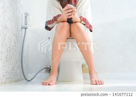 A woman sits on the toilet bowl in the bathroom, and she takes off her pants shorts in the bathroom. She had a stomach ache and was dissatisfied with constipation, diarrhea, food poisoning, 141077112