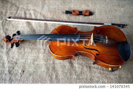 Classic wooden violin with bow and wooden bow tie on burlap Classic wooden violin with bow and wooden bow tie on burlap 141078345