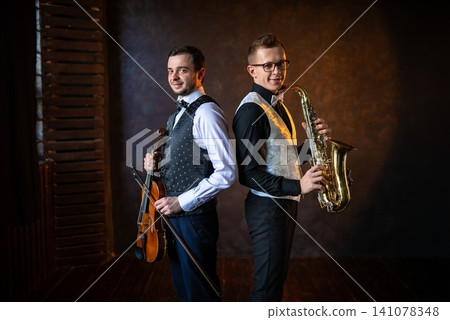 Duet of violinist and saxophonist standing back to back 141078348