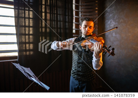 Expressive violinist performing indoors near a window Expressive violinist performing indoors near a window 141078359
