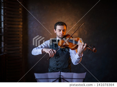 Male violinist playing instrument behind music stand 141078364