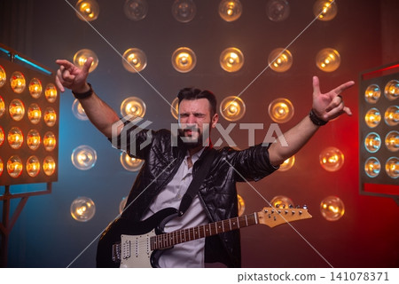 Expressive rock musician raising hands on stage Expressive rock musician raising hands on stage 141078371