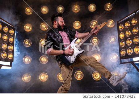 Rock guitarist performing dynamic kick on stage Rock guitarist performing dynamic kick on stage 141078422