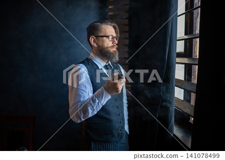 Intellectual man smoking a classic pipe by the window Intellectual man smoking a classic pipe by the window 141078499
