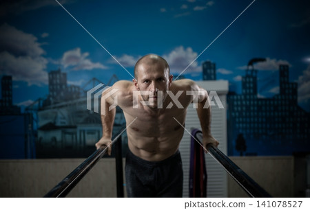 Athletic male performing dips on parallel bars at an indoor gym Athletic male performing dips on parallel bars at an indoor gym 141078527