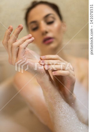 Woman examining soap foam on her hands in a tub Woman examining soap foam on her hands in a tub 141078531