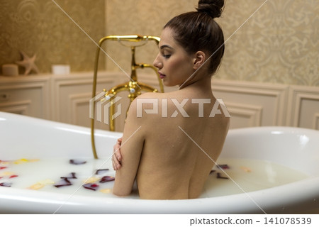 Sensual woman showing her bare back in a milk bath with petals Sensual woman showing her bare back in a milk bath with petals 141078539