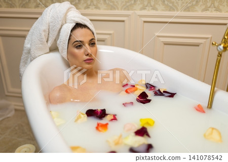 Thoughtful woman looking away while taking a milk bath with petals Thoughtful woman looking away while taking a milk bath with petals 141078542
