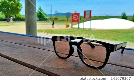 A scene of early summer: black-rimmed sunglasses placed on a wooden bench. A scene of early summer: black-rimmed sunglasses placed on a wooden bench. 141079367