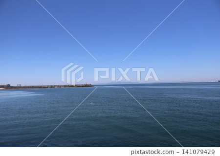 A seascape featuring a blue sky, hazy mountain ranges, a harbor dock, and the blue surface of the ocean. A seascape featuring a blue sky, hazy mountain ranges, a harbor dock, and the blue surface of the ocean. 141079429
