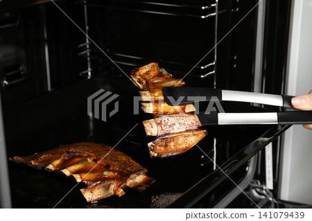 Woman taking delicious roasted ribs out of oven, closeup 141079439