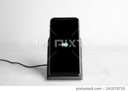 Mobile phone charging with wireless pad on light stone table Mobile phone charging with wireless pad on light stone table 141079710