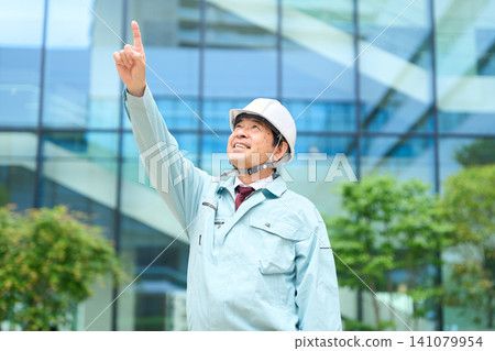 An Asian man in work clothes points his finger into the distance. An Asian man in work clothes points his finger into the distance. 141079954