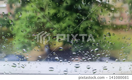 Raindrops on window glass with blurred green foliage background Raindrops on window glass with blurred green foliage background 141080081