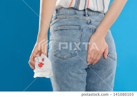 Woman holding toilet paper with blood stain on light blue background, closeup. Hemorrhoid concept Woman holding toilet paper with blood stain on light blue background, closeup. Hemorrhoid concept 141080103