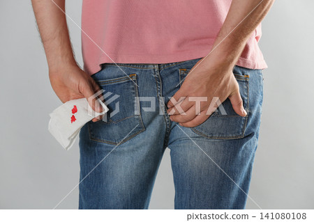 Man holding toilet paper with blood stain on light grey background, closeup. Hemorrhoid concept Man holding toilet paper with blood stain on light grey background, closeup. Hemorrhoid concept 141080108