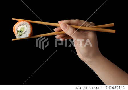 Woman holding sushi roll with chopsticks on black background, closeup Woman holding sushi roll with chopsticks on black background, closeup 141080141