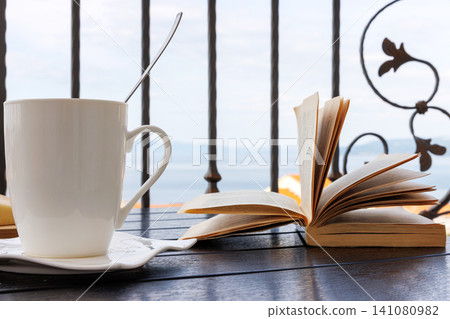 White coffee cup and open book on a balcony table overlooking the Adriatic Sea in Makarska, Croatia. White coffee cup and open book on a balcony table overlooking the Adriatic Sea in Makarska, Croatia. 141080982