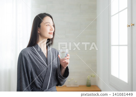 Young woman drinking water on the windowsill Young woman drinking water on the windowsill 141081449