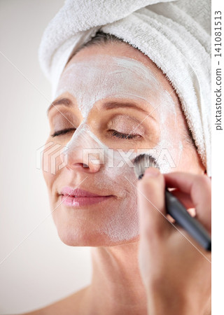 Beauty, mature woman and mask with brush in studio for skincare or anti aging on self care, wellness and fresh skin. Closeup, female person and glow with smile for facial and satisfied or luxury 141081513
