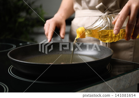 Woman pouring cooking oil from bottle into frying pan, closeup Woman pouring cooking oil from bottle into frying pan, closeup 141081654