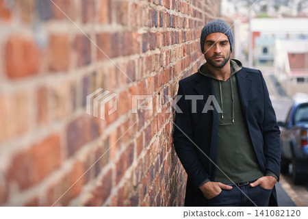 Portrait, confidence and man on brick wall in city in casual clothes, outfit or fashion for winter outdoor. Serious, cool and stylish person in urban town in beanie, hoodie and trendy jacket in Spain Portrait, confidence and man on brick wall in city in casual clothes, outfit or fashion for winter outdoor. Serious, cool and stylish person in urban town in beanie, hoodie and trendy jacket in Spain 141082120