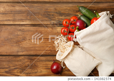 Cotton eco bags with vegetables and oat flakes on wooden table, flat lay. Space for text Cotton eco bags with vegetables and oat flakes on wooden table, flat lay. Space for text 141082374