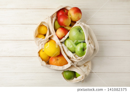 Cotton eco bags with fruits on white wooden background, flat lay Cotton eco bags with fruits on white wooden background, flat lay 141082375