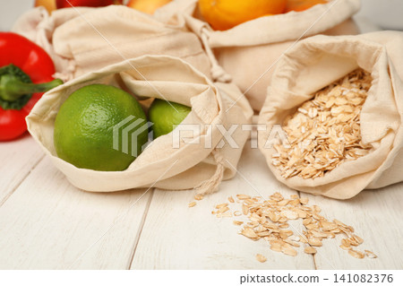 Cotton eco bags with fruits and oat flakes on white wooden table, closeup Cotton eco bags with fruits and oat flakes on white wooden table, closeup 141082376