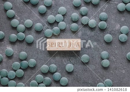 Horizontal top down flat lay shot of green spirulina chlorella algae tablets scattered on a dark grey stone background around a small wooden sign block Horizontal top down flat lay shot of green spirulina chlorella algae tablets scattered on a dark grey stone background around a small wooden sign block 141082618
