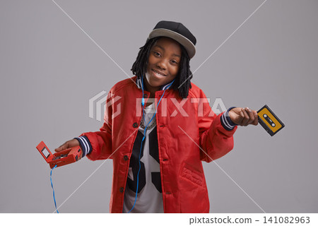 Music, shrug and child on gray background with cassette for listening to song, audio and radio. Fashion, youth and young African boy with retro tech for track playlist in trendy clothes in studio Music, shrug and child on gray background with cassette for listening to song, audio and radio. Fashion, youth and young African boy with retro tech for track playlist in trendy clothes in studio 141082963