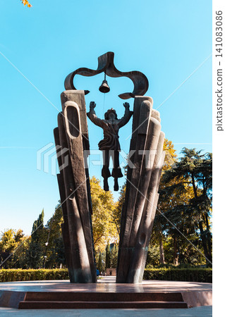 Modern bronze sculpture of a bell ringer with raised arms, standing in a park. Vertical Modern bronze sculpture of a bell ringer with raised arms, standing in a park. Vertical 141083086