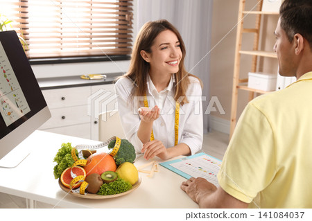 Young nutritionist consulting patient at table in clinic Young nutritionist consulting patient at table in clinic 141084037
