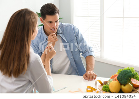 Young nutritionist consulting patient at table in clinic Young nutritionist consulting patient at table in clinic 141084054