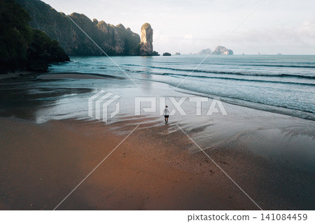 Lonely traveler walking on a pristine tropical beach at low tide with limestone islands, Krabi. Lonely traveler walking on a pristine tropical beach at low tide with limestone islands, Krabi. 141084459