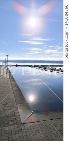 Bright sun reflecting on smooth water, sun, clouds, pier, embankment Bright sun reflecting on smooth water, sun, clouds, pier, embankment 141084566