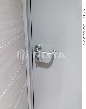 Modern stainless steel door handle and lock on a white door with light wood paneling visible in the background, showcasing contemporary interior design elements Modern stainless steel door handle and lock on a white door with light wood paneling visible in the background, showcasing contemporary interior design elements 141085100
